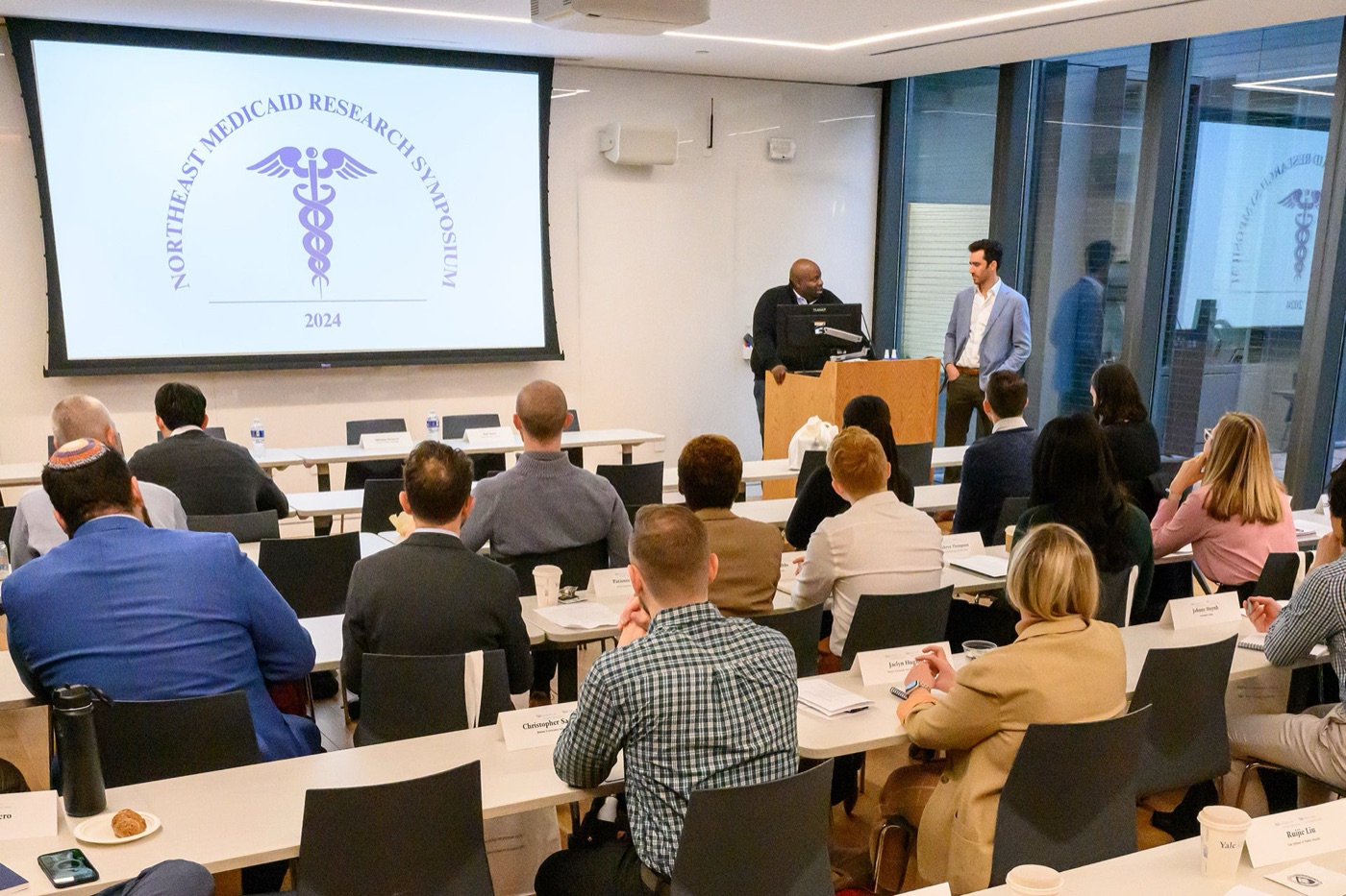 Chima Ndumele and Jacob Wallace at the lectern opening the 2024 Northeast Medicaid Research Symposium at Yale